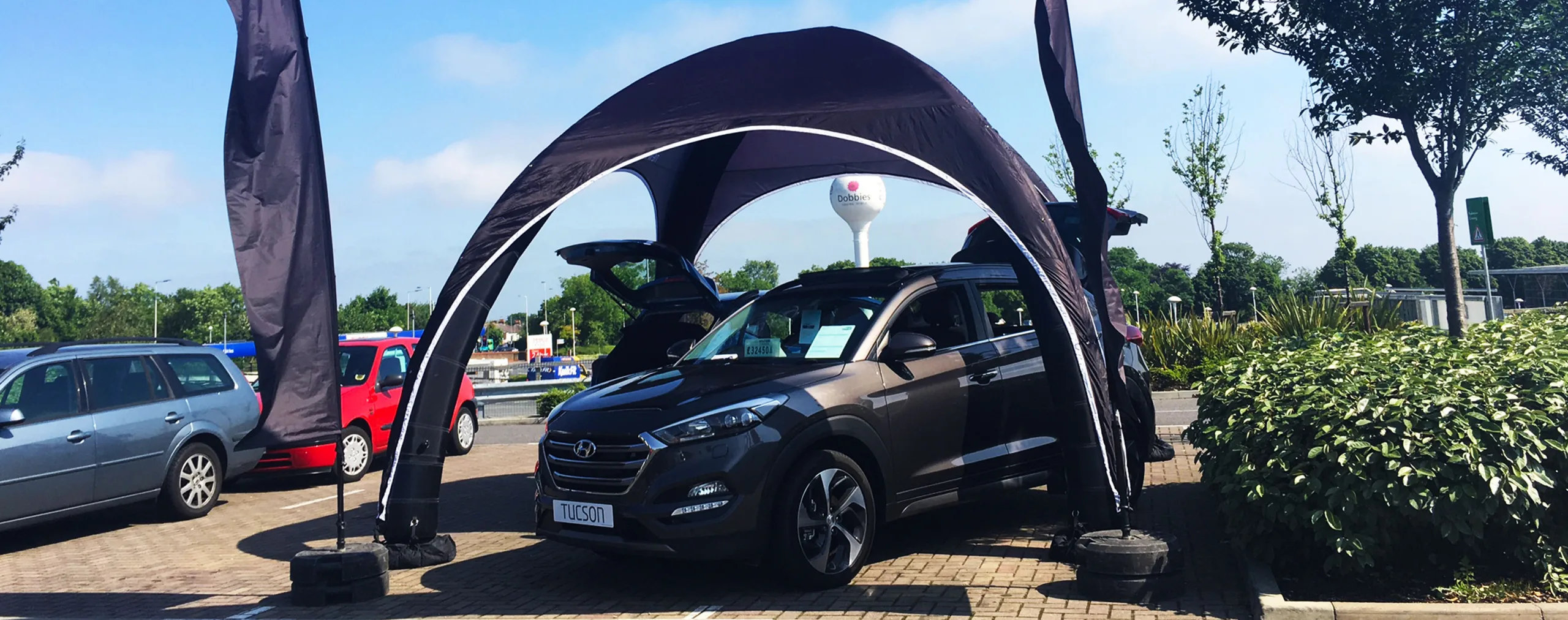 Pic showing a Created By Air custom branded structure X tent used to cover a car at a promotion area display